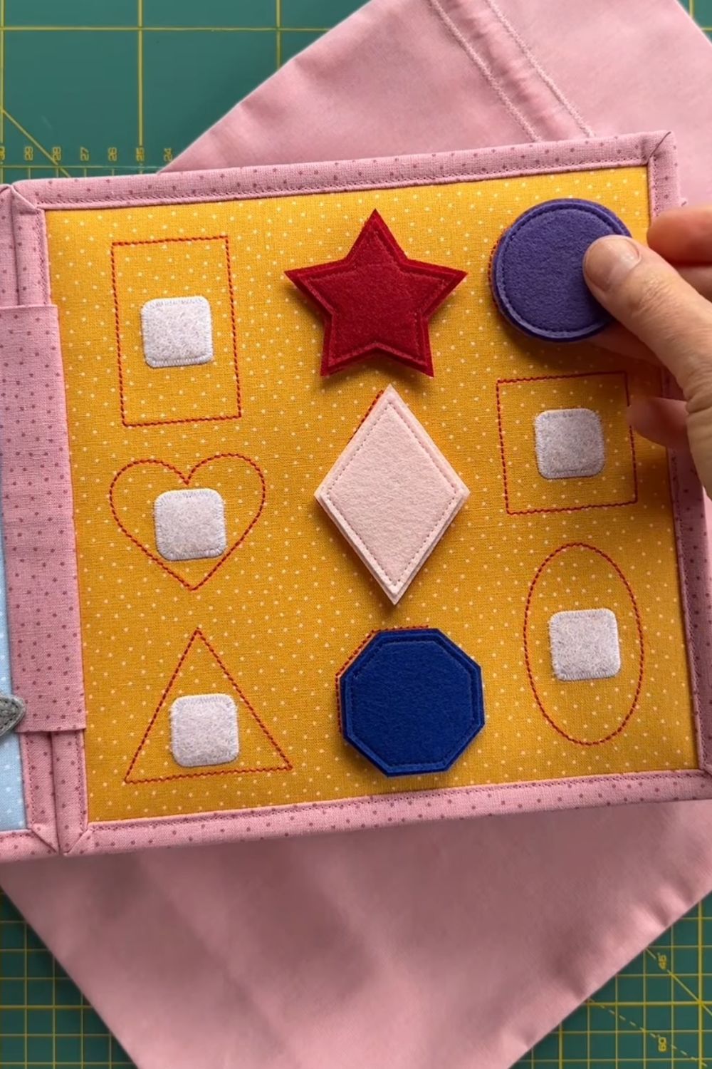 A colorful felt quiet book page with shapes like circles, squares, and triangles for toddlers to match